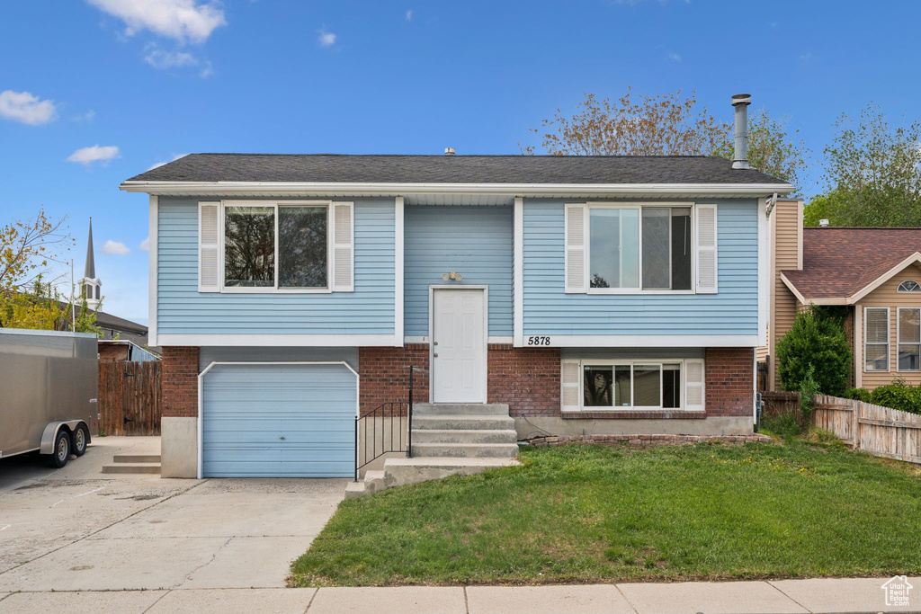 Raised ranch featuring an attached garage, concrete driveway, brick siding, and entry steps
