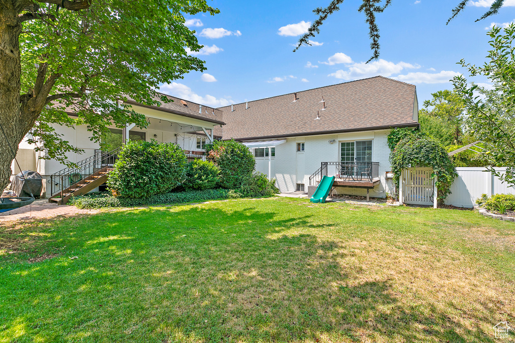 Back of property featuring roof with shingles, stairs, fence, a deck, and a yard