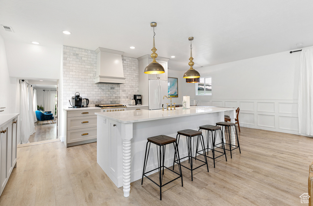 Kitchen with a kitchen breakfast bar, a kitchen island with sink, visible vents, wall chimney exhaust hood, and light wood finished floors