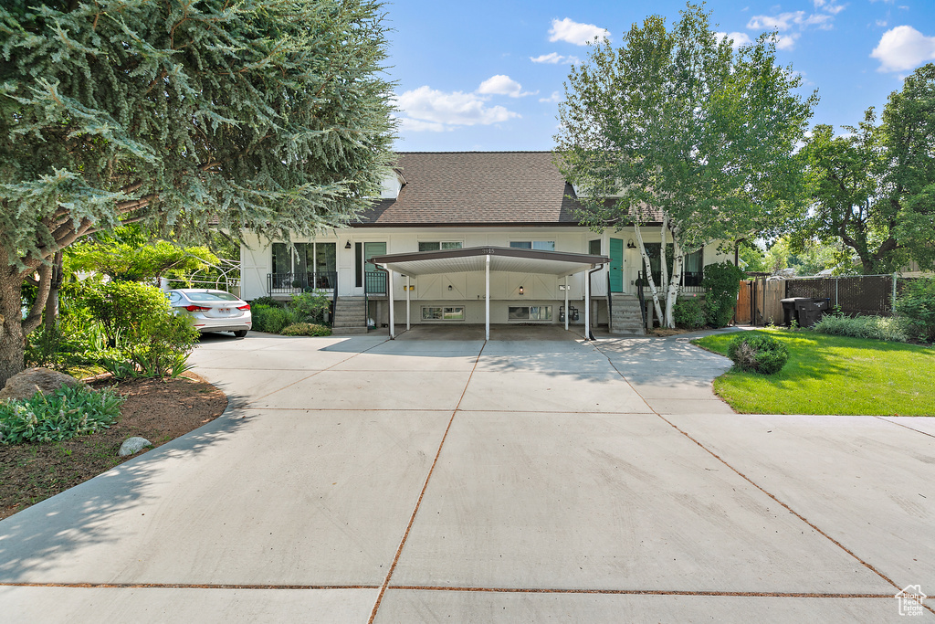 View of front of home featuring concrete driveway, roof with shingles, fence, and a carport