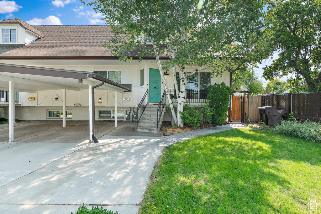 Townhome / multi-family property with driveway, fence, a shingled roof, a front yard, and a carport