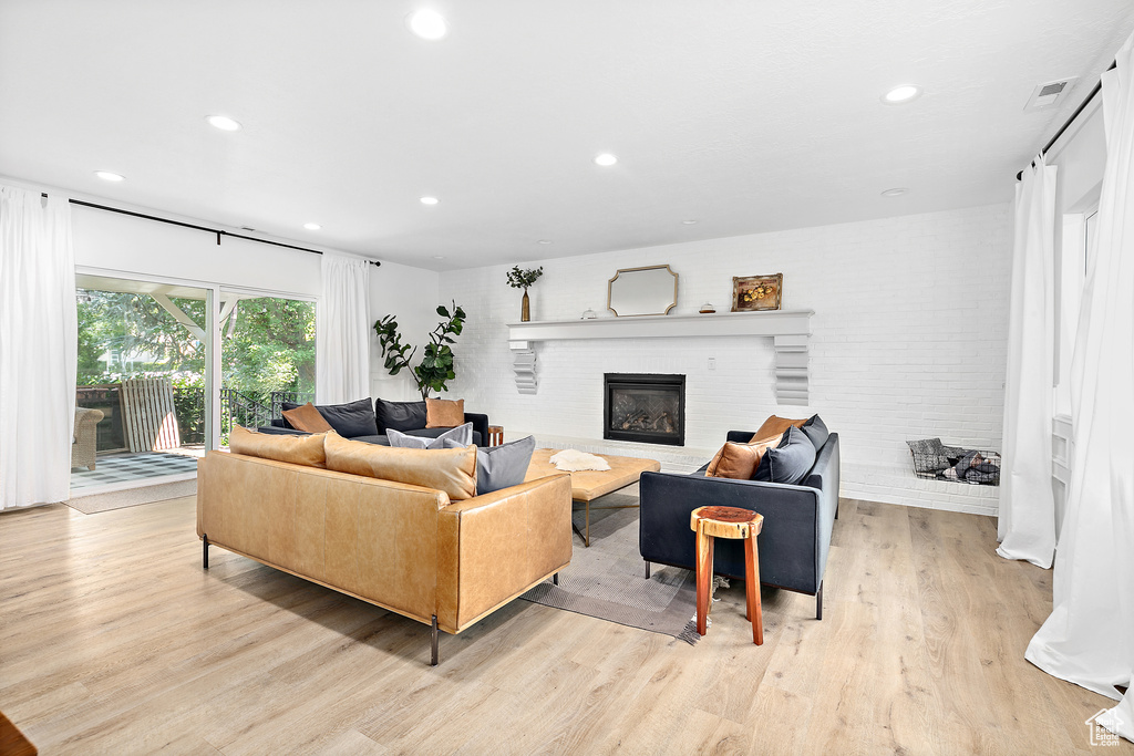 Living area with a brick fireplace, light wood-style flooring, and recessed lighting