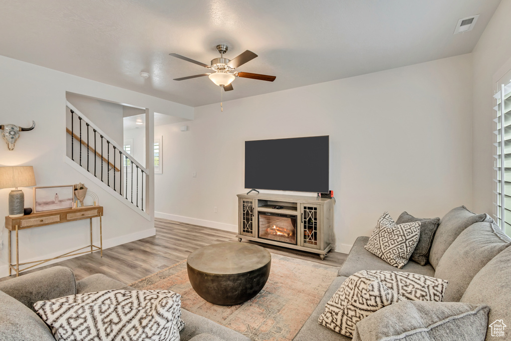 Living room with ceiling fan, wood finished floors, stairs, and baseboards