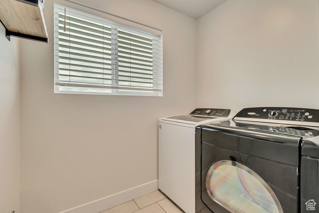 Washroom featuring separate washer and dryer, light tile patterned flooring, and baseboards