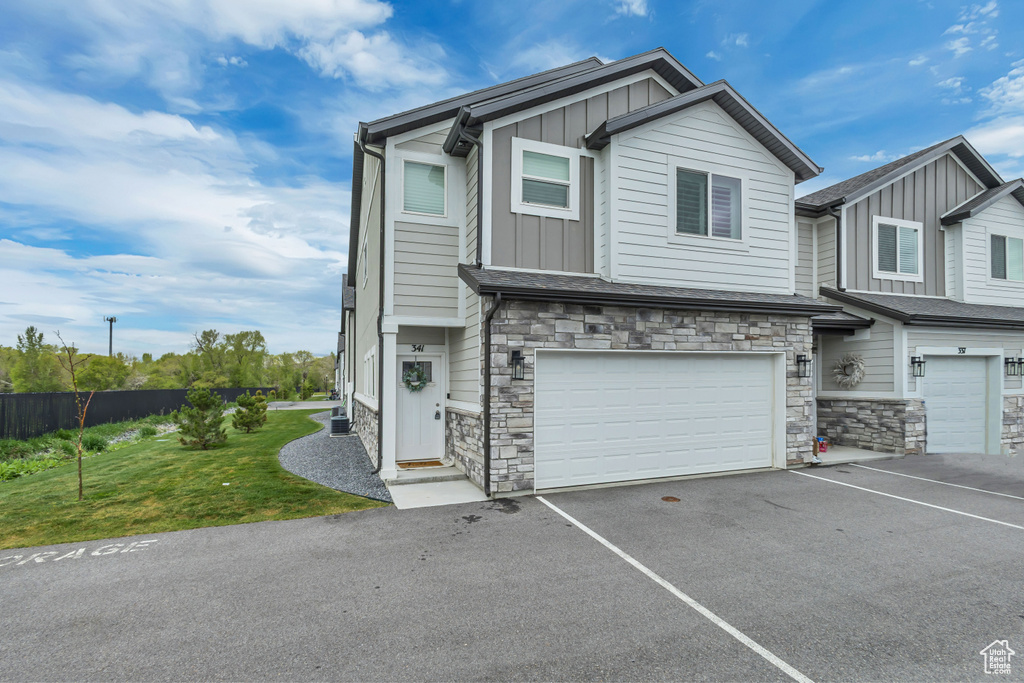 Multi unit property with board and batten siding, stone siding, a garage, and asphalt driveway