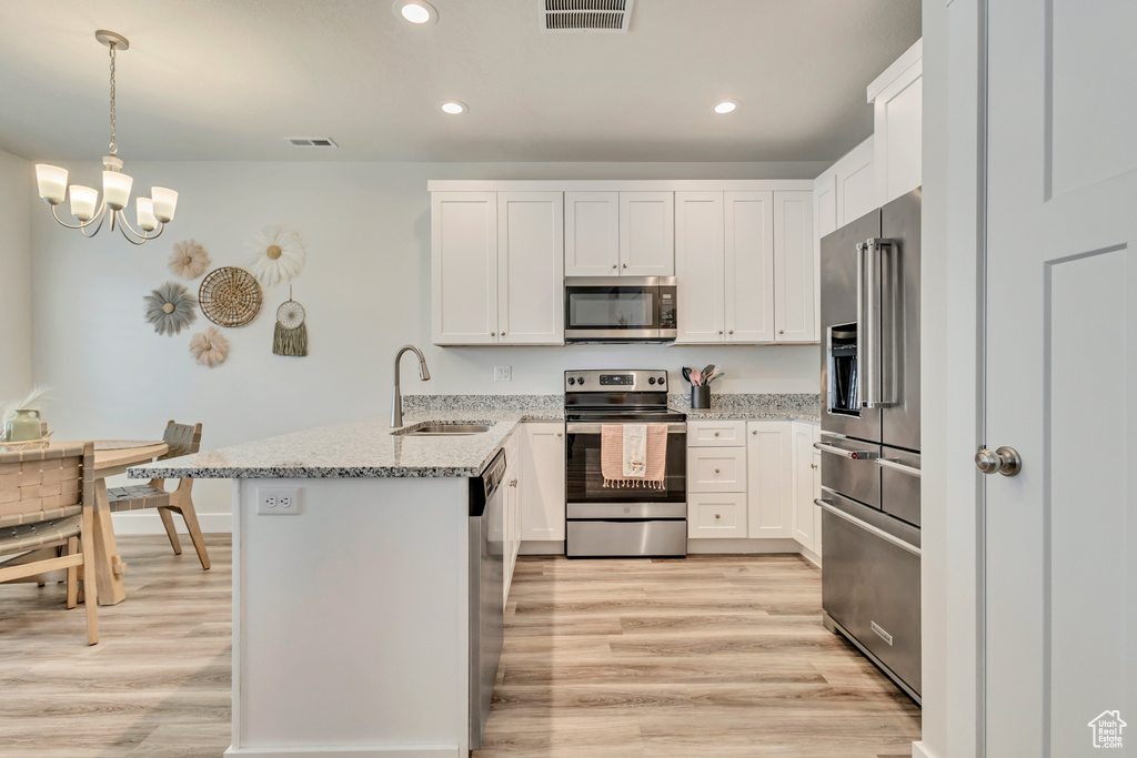 Kitchen featuring stainless steel appliances, a sink, a peninsula, light wood-style floors, and recessed lighting