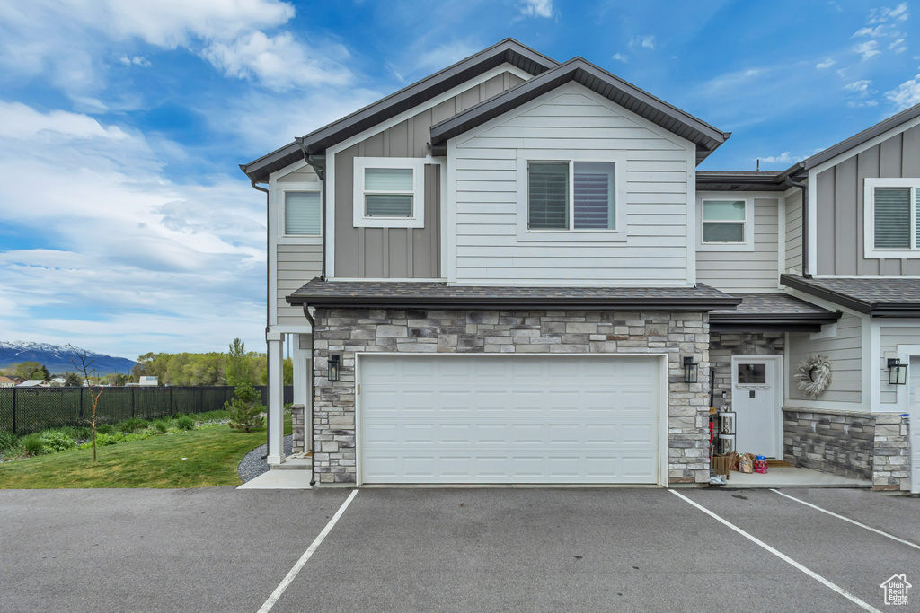 Multi unit property featuring board and batten siding, stone siding, driveway, an attached garage, and a mountain view