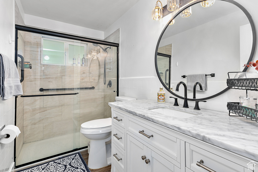 Bathroom featuring toilet, a stall shower, tile walls, a chandelier, and vanity