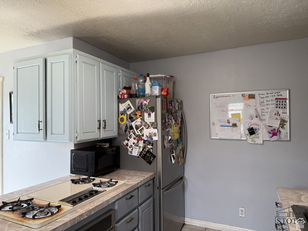 Kitchen featuring black microwave, freestanding refrigerator, white gas stovetop, light countertops, and a textured ceiling