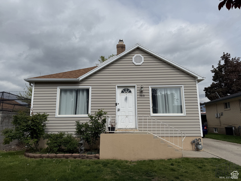 Bungalow-style home with a chimney, central AC unit, and a front yard
