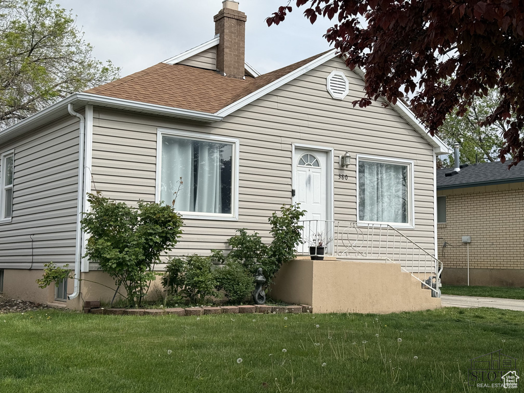 View of front of property featuring a front yard, a chimney, and roof with shingles