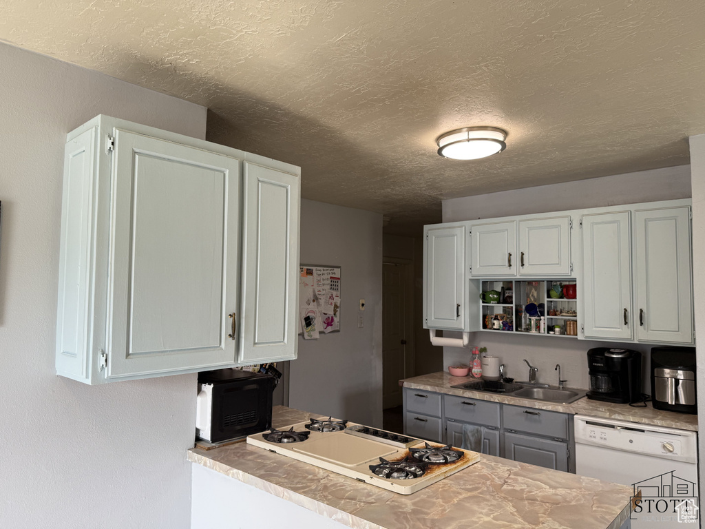 Kitchen featuring white appliances, a sink, a textured ceiling, white cabinetry, and light countertops