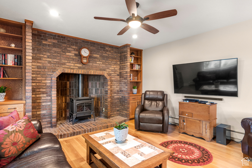 Living room featuring a wood stove, a ceiling fan, light wood-style floors, and a baseboard radiator