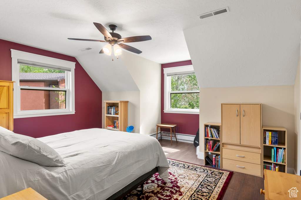 Bedroom with lofted ceiling, wood finished floors, a ceiling fan, a baseboard heating unit, and baseboards