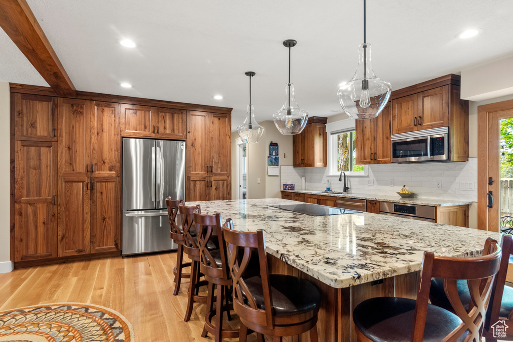 Kitchen with appliances with stainless steel finishes, decorative backsplash, light wood-style floors, recessed lighting, and brown cabinets
