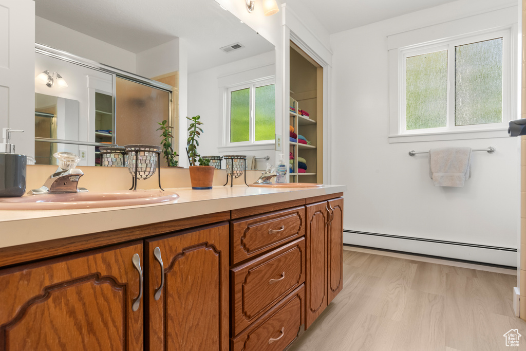 Full bathroom featuring a baseboard radiator, an enclosed shower, double vanity, and wood finished floors