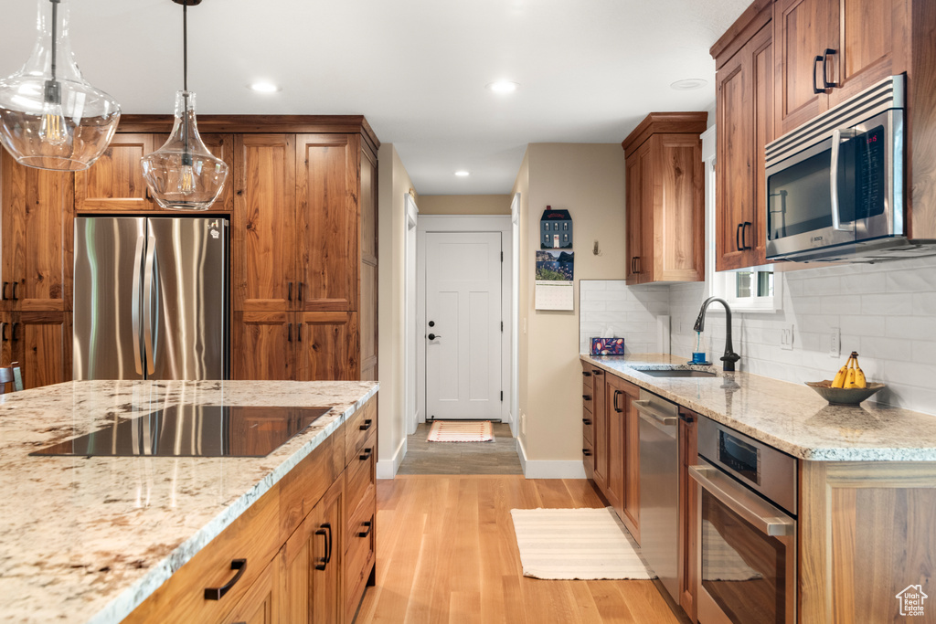 Kitchen featuring appliances with stainless steel finishes, a sink, light wood-type flooring, brown cabinetry, and recessed lighting