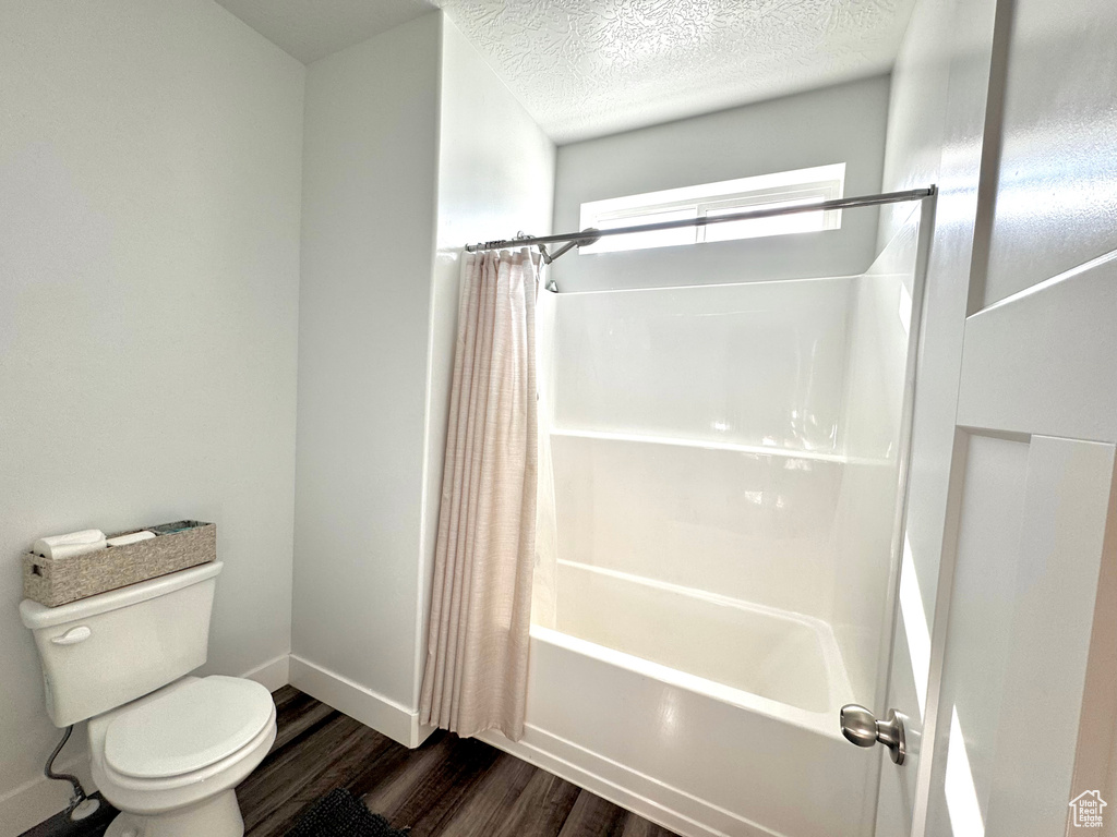 Full bath with toilet, wood finished floors, a textured ceiling, baseboards, and shower / bathtub combination with curtain