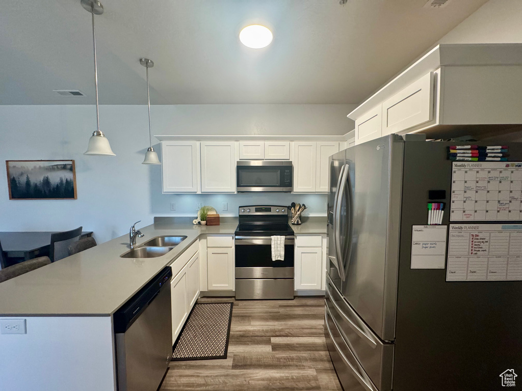 Kitchen with a sink, white cabinetry, a peninsula, wood finished floors, and appliances with stainless steel finishes