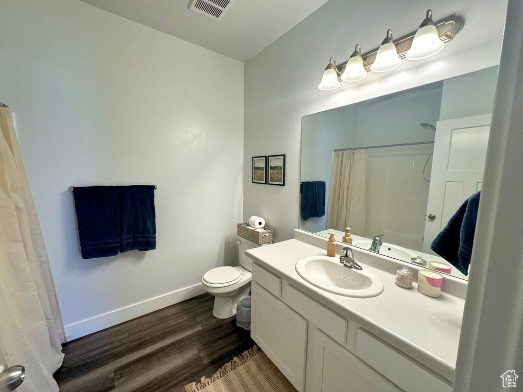 Bathroom with toilet, wood finished floors, vanity, visible vents, and baseboards