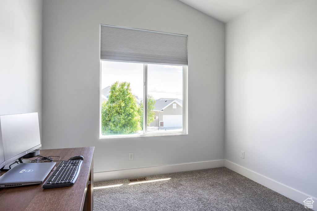 Carpeted empty room with healthy amount of natural light, baseboards, vaulted ceiling, and a desk
