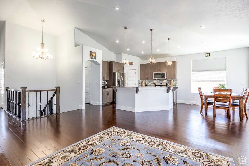 Kitchen with appliances with stainless steel finishes, a kitchen bar, dark wood finished floors, a chandelier, and recessed lighting