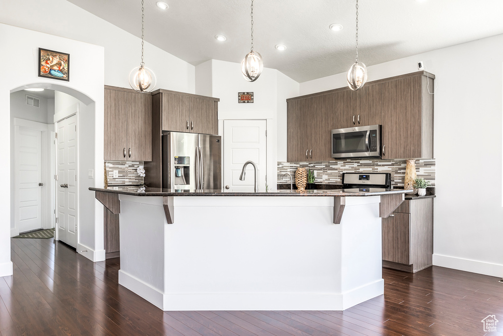 Kitchen with appliances with stainless steel finishes, arched walkways, a kitchen breakfast bar, tasteful backsplash, and dark wood-style flooring