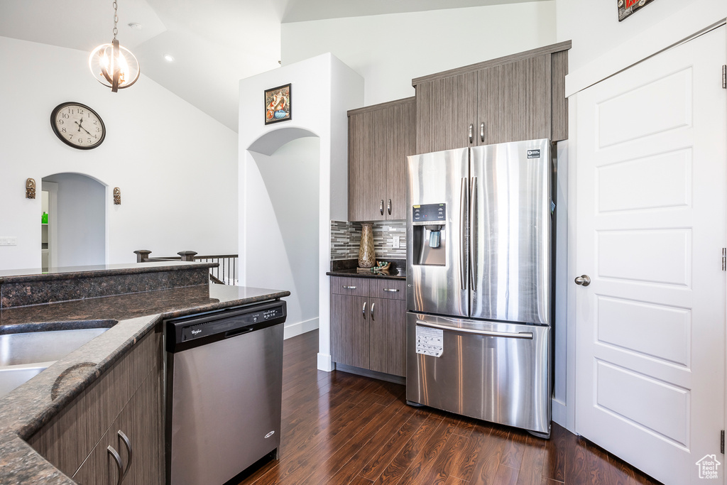 Kitchen featuring stainless steel appliances, arched walkways, decorative backsplash, dark wood-type flooring, and dark stone counters