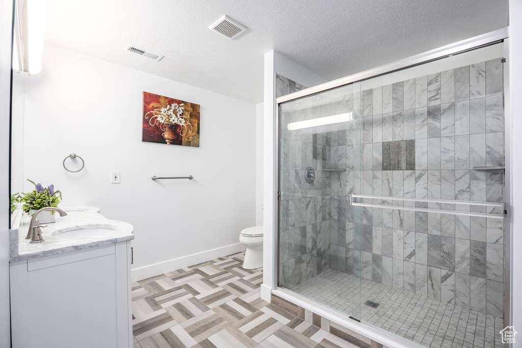 Full bath with a stall shower, baseboards, toilet, double vanity, and a textured ceiling