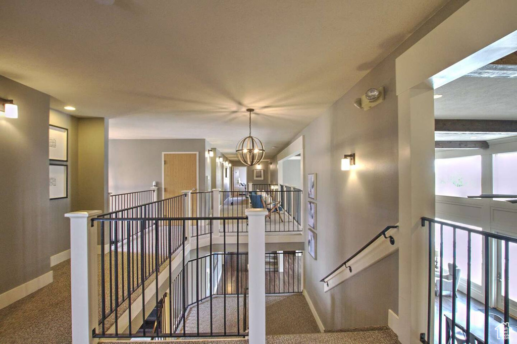 Hall with baseboards, a notable chandelier, an upstairs landing, and carpet