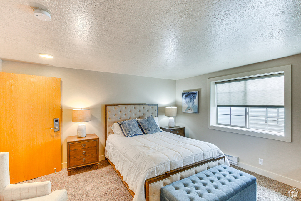 Carpeted bedroom featuring baseboards, baseboard heating, and a textured ceiling