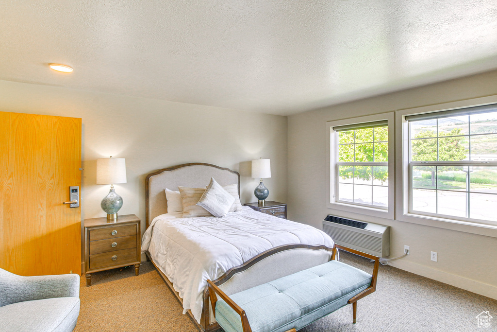Bedroom featuring a textured ceiling, carpet floors, a wall unit AC, and baseboards