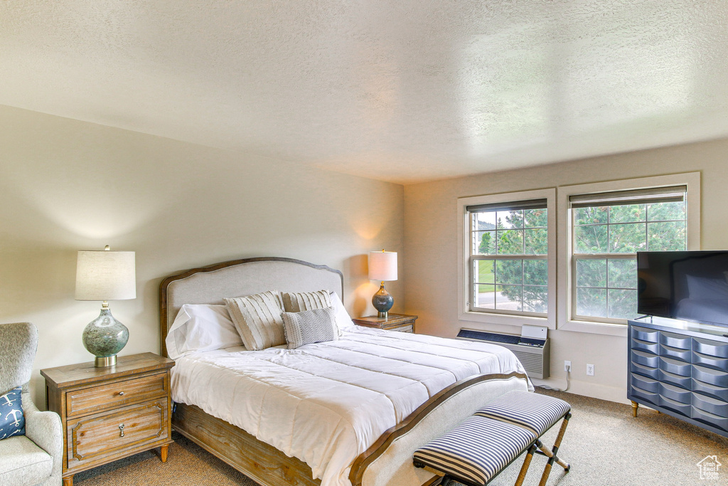 Bedroom with baseboards, carpet flooring, a wall mounted air conditioner, and a textured ceiling