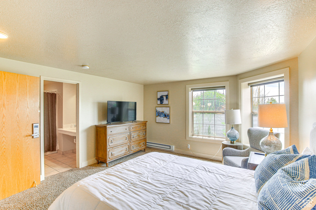 Bedroom with a textured ceiling, a baseboard heating unit, baseboards, light tile patterned floors, and ensuite bath