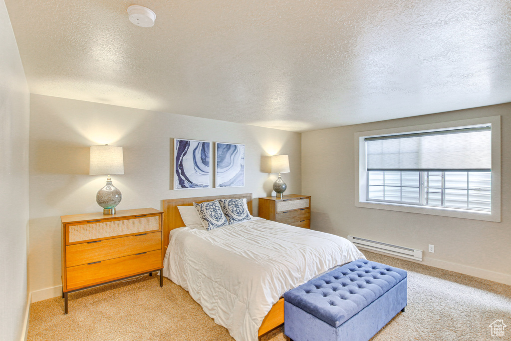 Carpeted bedroom featuring a baseboard heating unit, baseboards, and a textured ceiling