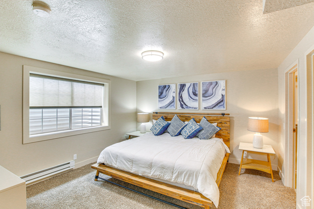 Bedroom featuring a textured ceiling, carpet, baseboards, and a baseboard heating unit