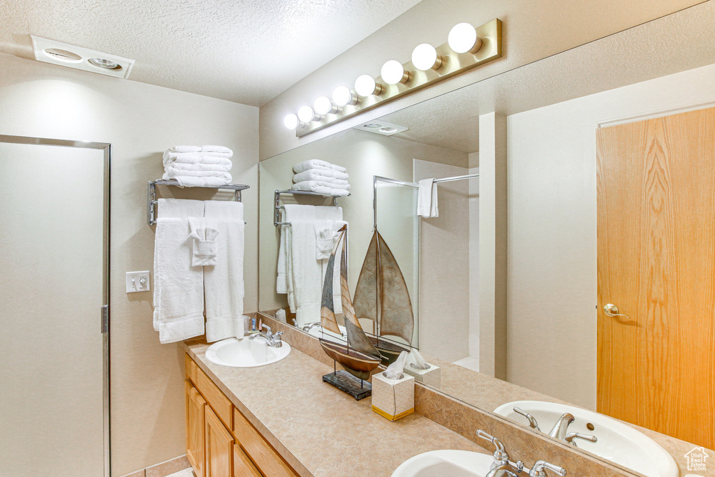 Full bath featuring a textured ceiling, double vanity, a sink, and a shower stall