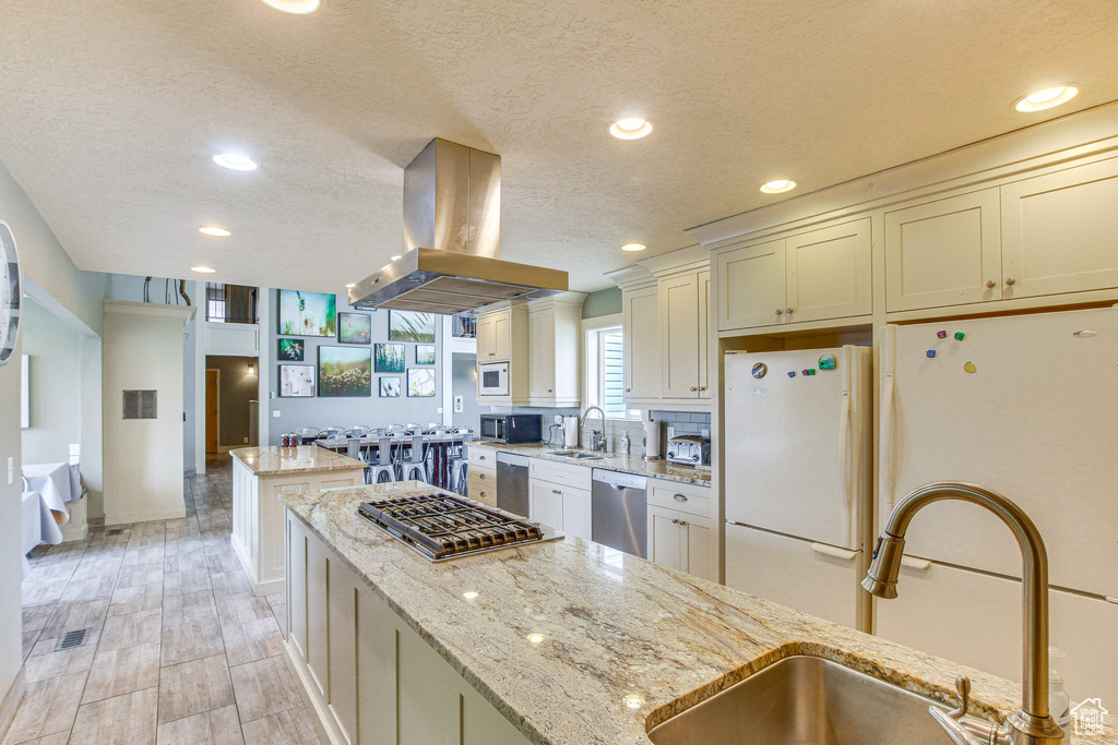 Kitchen featuring a sink, stainless steel appliances, island exhaust hood, a textured ceiling, and a kitchen island