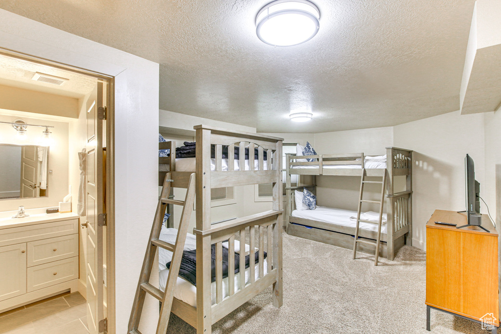 Bedroom with light carpet, connected bathroom, visible vents, and a textured ceiling