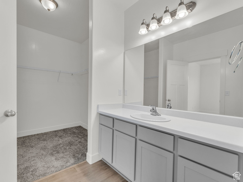 Full bathroom featuring a spacious closet, vanity, baseboards, and wood finished floors