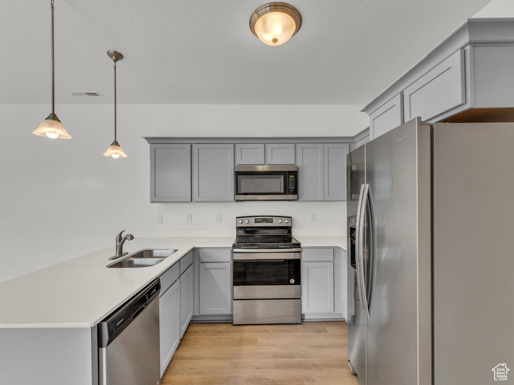 Kitchen featuring appliances with stainless steel finishes, a sink, gray cabinetry, a peninsula, and light countertops