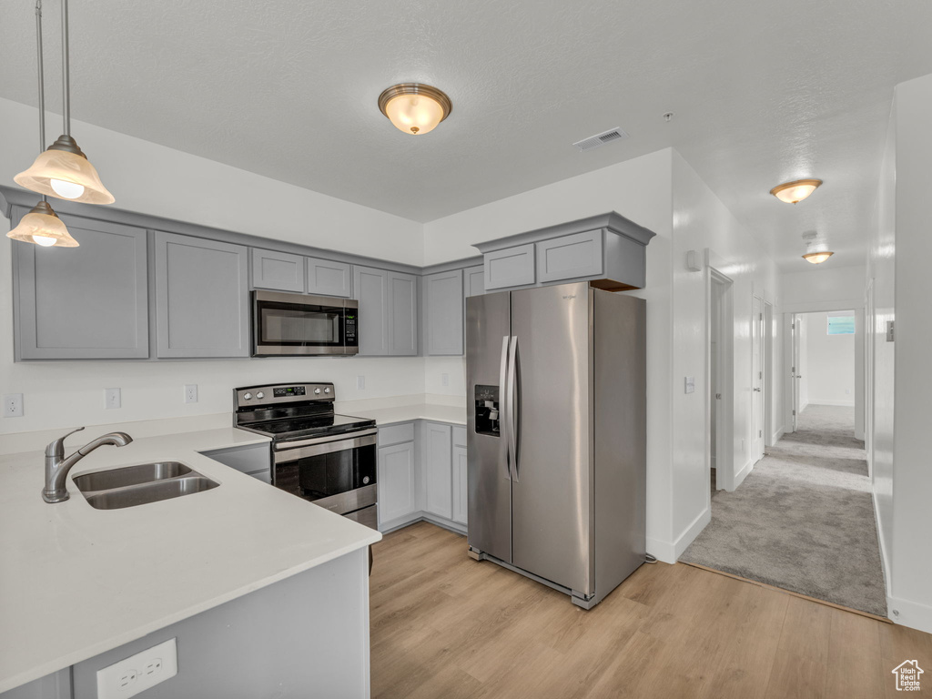 Kitchen with appliances with stainless steel finishes, a sink, gray cabinetry, light wood-style flooring, and light countertops