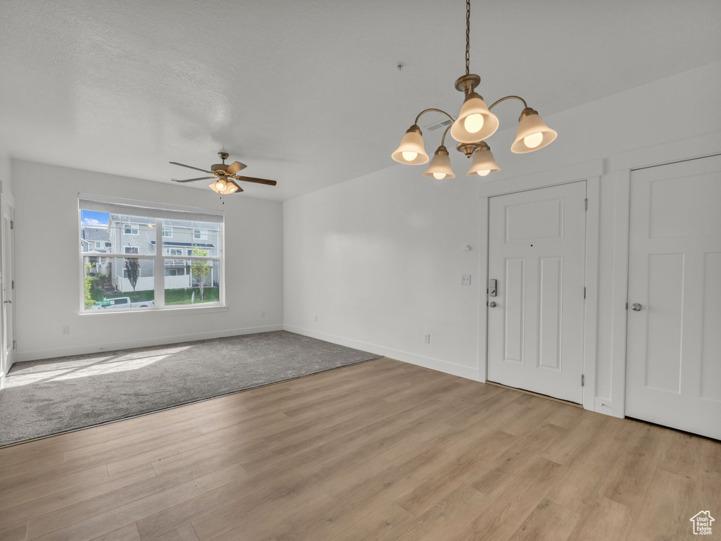 Unfurnished living room featuring light wood-type flooring, a chandelier, a ceiling fan, and baseboards