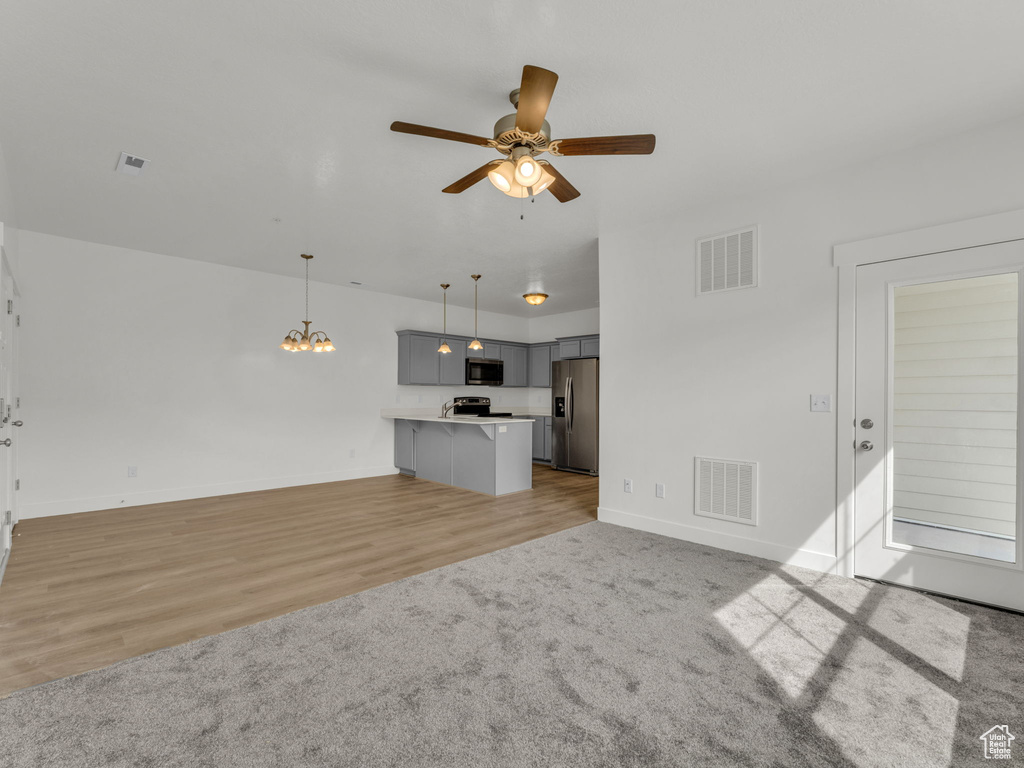 Unfurnished living room with a ceiling fan, baseboards, a chandelier, and light wood-style flooring