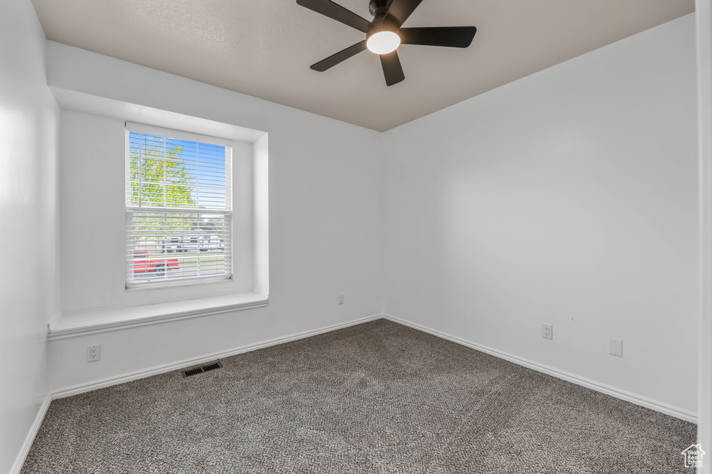 Empty room featuring dark colored carpet, ceiling fan, and baseboards
