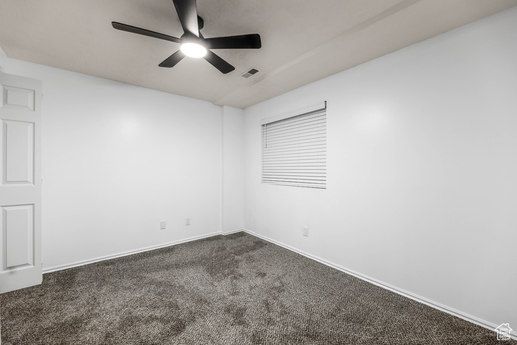 Unfurnished room featuring dark carpet, ceiling fan, and baseboards
