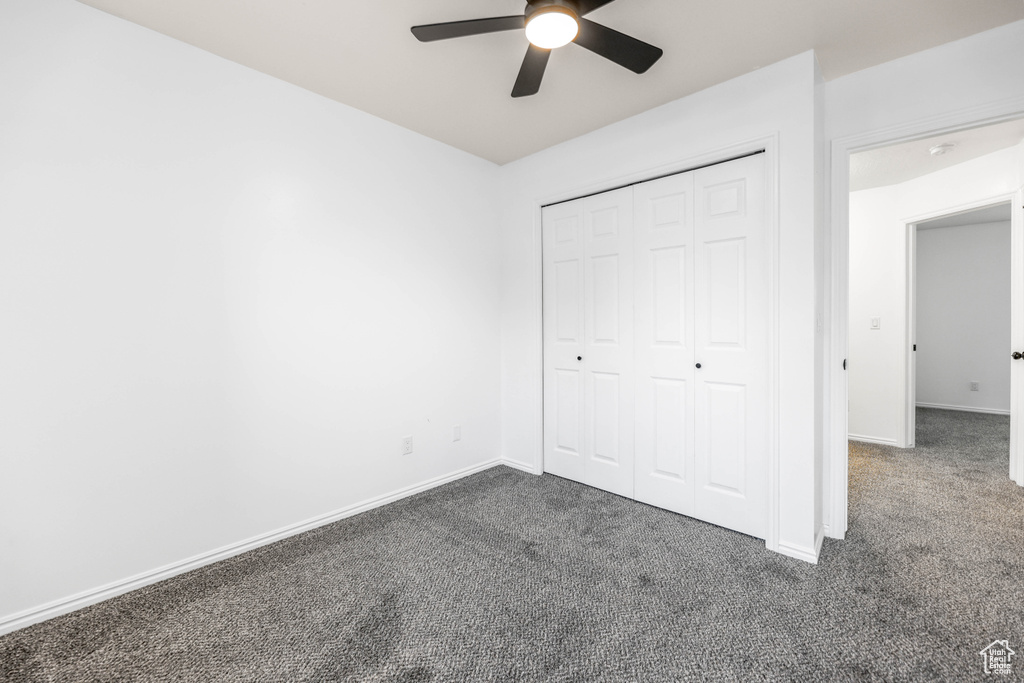 Unfurnished bedroom with dark colored carpet, baseboards, a closet, and a ceiling fan