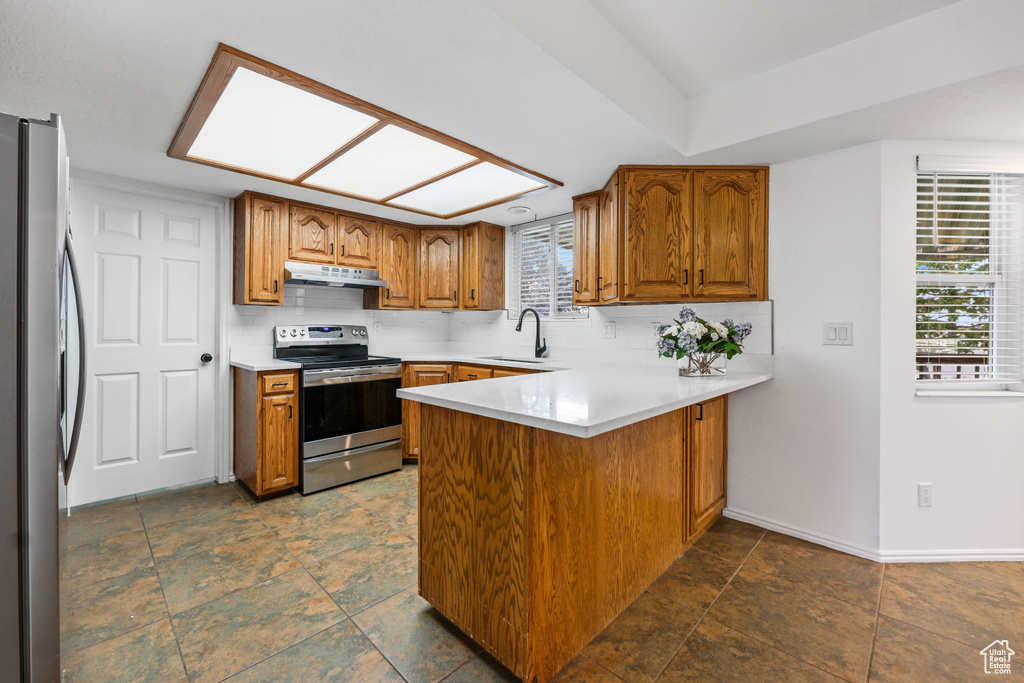 Kitchen featuring appliances with stainless steel finishes, under cabinet range hood, a sink, a peninsula, and brown cabinets