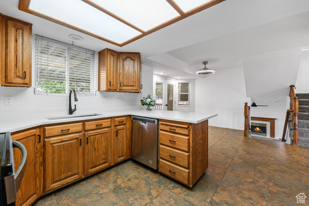 Kitchen featuring a sink, dishwasher, a peninsula, and brown cabinetry