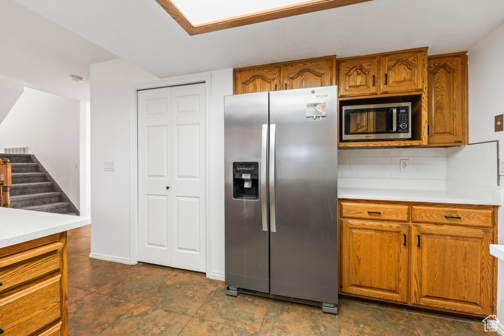 Kitchen with stainless steel appliances, brown cabinetry, light countertops, tasteful backsplash, and baseboards